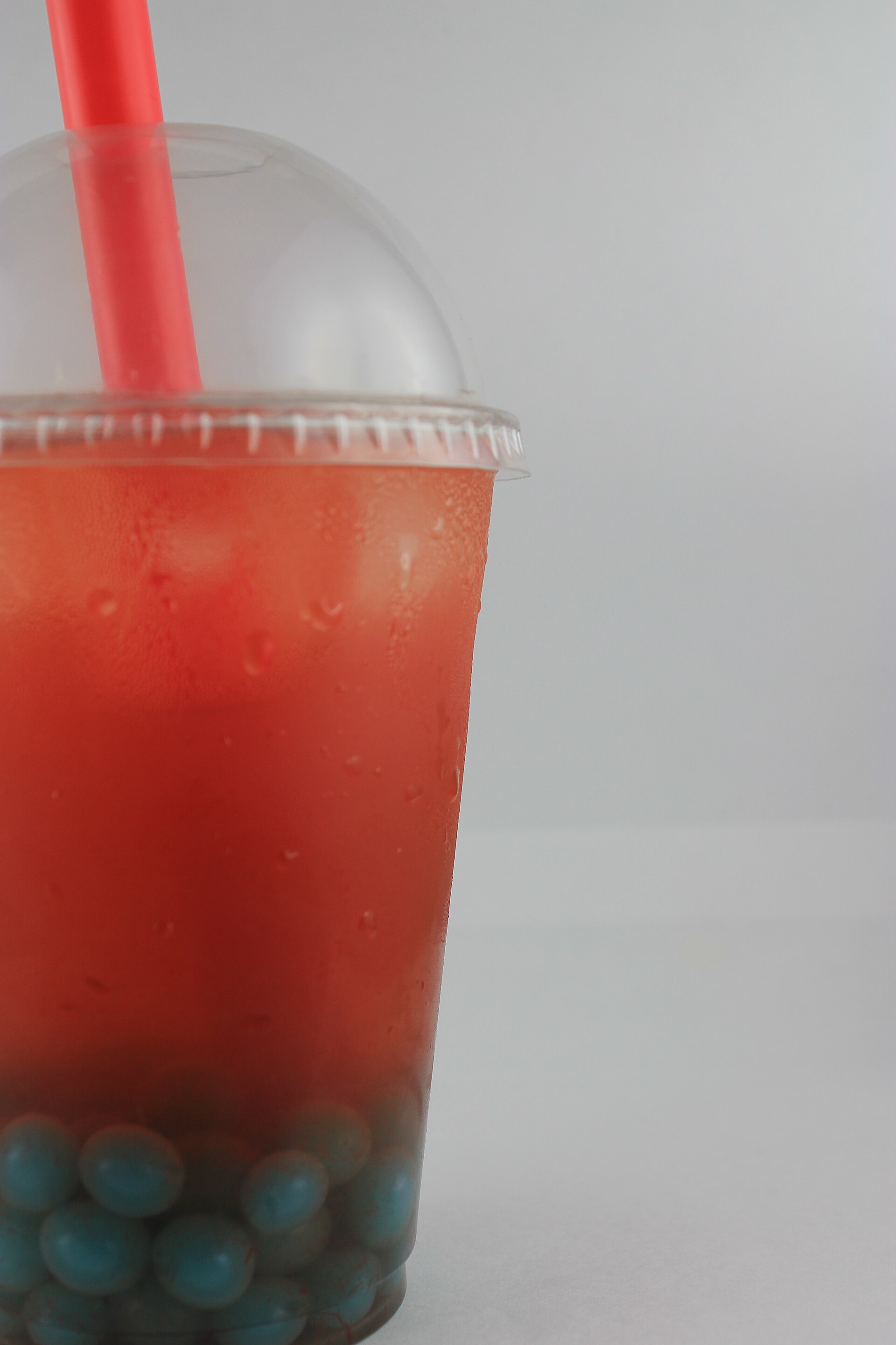 A tall cup of red fruit tea with a domed lid