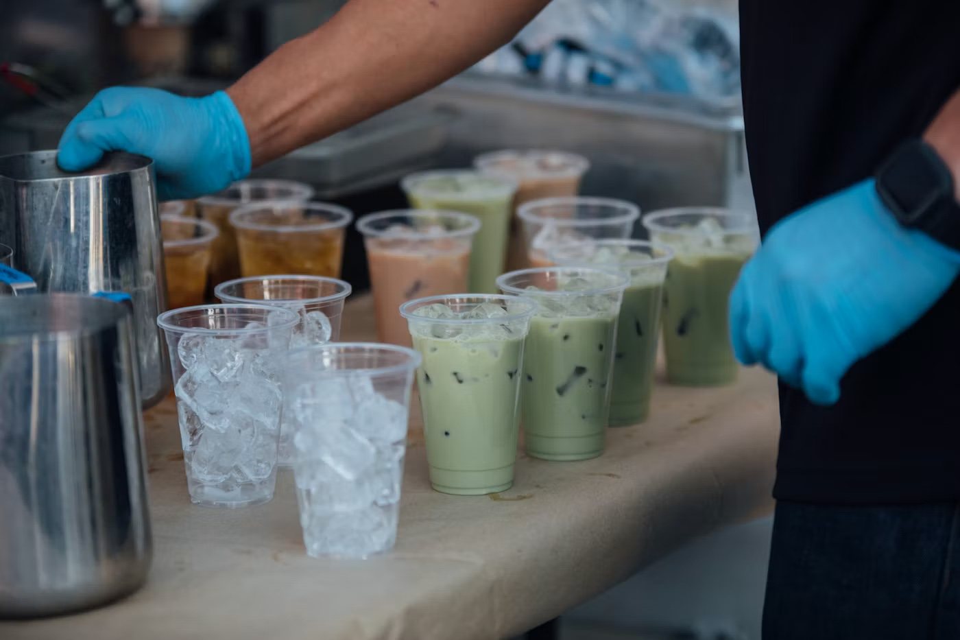 A gloved server behind a row of freshly made iced teas at an event