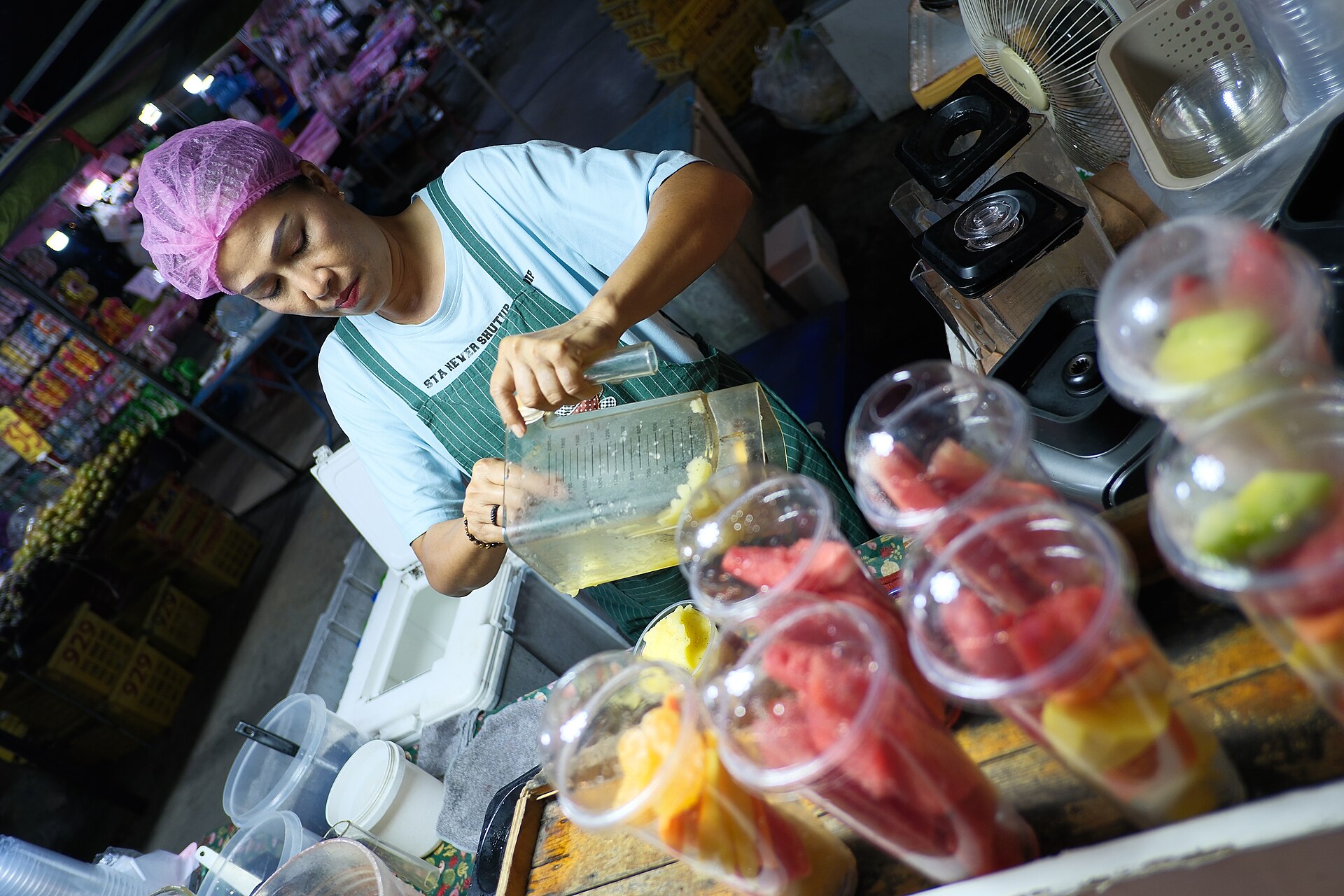 A vendor pouring fresh fruit into a blender at a market stall